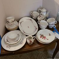 Photo of entire china set on wooden table showing teacups, saucers, plates, small pitcher, oval serving platter, and teapot with matching floral designs and gold trim.