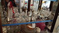 Photo shows Dura Best handmade music boxes, glass candle holders, assorted glassware and a glass stein on glass shelving.