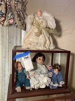 Full view of the display box with four porcelain dolls inside and the angel figurine on top