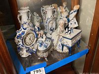 Overall view of the porcelain figurines, clock, and vases on glass shelf with blue painter's tape visible