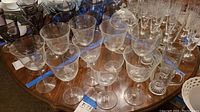 Collection of clear crystal wine glasses with long stems and etched floral and wheat designs on the bowl, arranged on a table.