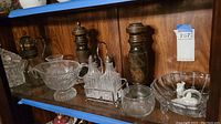 Shelved collection of several vintage glass and metal items including crystal bowl, condiment caddy, pepper mills, and glass bowl with animal figurine
