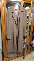 Full front view of vintage long brown tweed wool coat hanging on a wooden door, showing its length and texture.