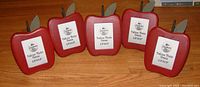 Set of five red wooden apple-shaped photo frames displayed together on a wooden floor.