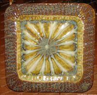 Top-down view of the square glazed pottery ashtray with yellow and green cycledelic design and textured border.