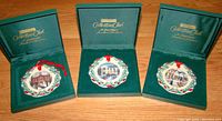 Three hand-painted fine vitrified china ornaments displayed in original green velvet-lined Longaberger Collectors Club boxes. Each ornament features a colorful holiday scene with holly and ribbon detailing.