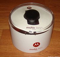 Top view of sealed round Motorola Moto 360 Sport packaging showing watch inside clear plastic top with white base labeled with Moto 360 Sport and Motorola logo.