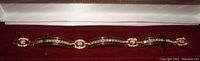 Full front view of the gold tone bracelet showing alternating black baguette rhinestones and clear round rhinestones on a burgundy velvet background.
