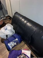 Black inflatable air mattress, blue sleeping bag rolled, and white drawstring bag on a floor surface