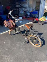 Side and rear angle view of Citizen 16 inch black bicycle with brown seat, attached wicker basket and travel bag, parked in driveway.