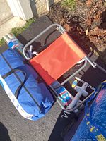 Outdoor photo of red fabric beach chair, blue rolled tent bag, white manual pump, and Igloo wheeled cooler