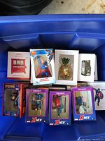 Photo of multiple Hallmark Keepsake ornaments and Marvel superhero ornaments in their original boxes, arranged on a blue container lid.
