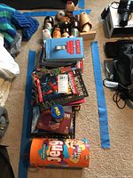 Photo of wooden Asian dolls and assorted books, games stacked on floor.