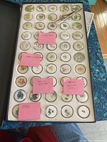 Top view of the gemstone sample case showing various small loose gemstones under circular clear covers with stickers labeling some stones as 'white topaz,' 'smoky quartz,' 'yellow sapphire,' 'citrine garnet topaz,' and 'topaz'.