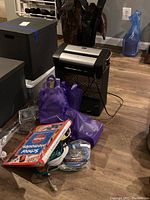 Photo showing the office paper shredder, purple bags with cords, black storage boxes, and candles.