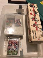 Photo of sports cards inside a plastic container and loose cards outside, showing football players.
