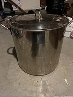 Full view of the stainless steel brew pot with lid on, showing two side handles and a reflective surface.