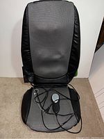 Full view of the electric back massager cushion showing gray mesh and black faux leather sides with wired remote control on seat area.