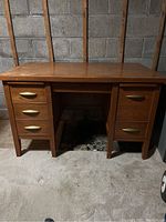 Front view of wooden bankers desk showing four drawers on left and one drawer plus cabinet door on right, with brass colored handles.
