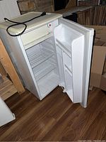White Danby bar fridge open showing interior with freezer compartment, wire shelves, and door shelves.