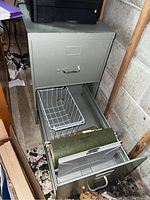 Front view of gray metal filing cabinet with open drawers showing wire basket and hanging file racks with folders.