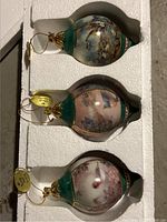 Three Lena Liu porcelain Christmas ornaments in original styrofoam packaging, showing upper, middle, and lower ornaments with bird and nature scenes.
