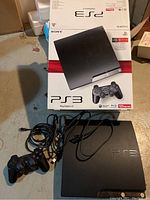 Sony PlayStation 3 console with one black controller, power cord, and original box with 120GB branding on floor.