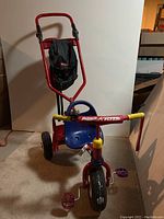 Front view of the red Radio Flyer tricycle showing the yellow handle grips, blue seat, and black adjustable parent handle with red holster.