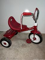 Side angle showing red seat, handlebar with tassels, and three black and white wheels