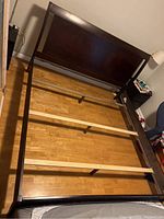 King size wooden bed frame fully assembled on floor, showing headboard and side rails with slats, visible scratches on wood edges.