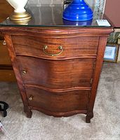 Front view of antique wooden side table with bow front, brass hardware, and removable glass top.