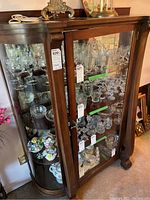 Front and left side view of two-door hardwood china cabinet showing curved glass side panels and three interior glass shelves.