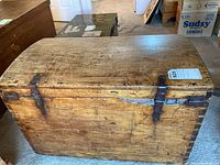 Front and top view of the wooden storage trunk showing metal latch hardware and worn wood surface.