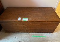 Top angled view of the large antique wooden storage trunk showing grain, condition, and size in relation to carpet.