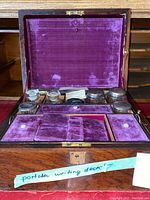Open wooden portable writing box showing purple velvet lining and compartments