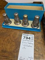 Photo showing four Birks sterling silver salt shakers in a blue lined box, arranged side by side on a table.