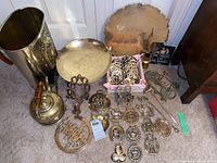 Photo of multiple brass items including trays, horse brasses, a decorative basket, candle snuffer, kettle and other brass decor items arranged on carpeted floor.