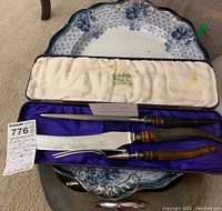 Overview of porcelain serving platter with ornate blue and white floral design, scalloped edges, with carving set box placed on top on carpet.
