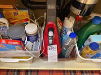 Shelf showing assorted cleaning supplies including SOS pads, Goddard's Silver Polish, Black & Decker handheld vacuum, and other bottles.