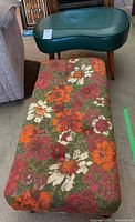 Two ottomans displayed side by side on carpet: rectangular floral fabric ottoman in front, green kidney-shaped faux leather ottoman behind.
