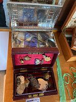 Wooden jewelry box open with red velvet interior showing pins and medals, silver-toned tin box behind.