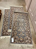 Three rugs stacked showing full length and fringe ends, light blue with floral and ornate beige and brown designs