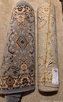 Two rolled runners standing upright showing front and back design and a tag on the beige runner, indicating size and lot number