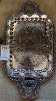 Large silver-plated rectangular tray with decorative handles and intricate embossed floral patterns. The tray is heavy and shows reflective shining surfaces.