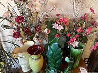 Front view of several vases holding faux flowers including Crown Devon pitcher and green pottery pieces