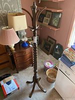 Full view of vintage wooden coat rack displaying twisted central pole, multiple hooks for hanging, and four-legged base on carpeted floor.