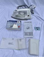 Rowenta replacement soleplate in box, user manual, warranty booklet and white iron rest holder displayed alongside iron on white background