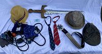 Photo of the entire lot on a white surface showing hats, ties, sword, belt and blood pressure cuffs laid out for display.