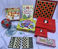 Full view of all lot items including board games, soccer ball, science kits, checkers game, and ceramic plate.