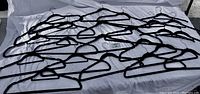 23 black velvet non-slip hangers spread out on a white sheet showing their slim profile and velvet coating.